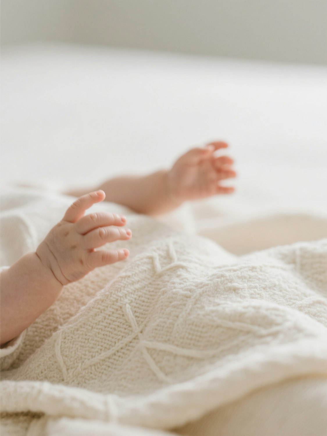 Tiny baby hands reaching out over a cream crocheted blanket